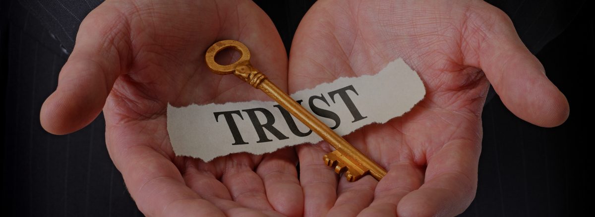Manos abiertas sosteniendo una llave dorada sobre un papel con la palabra Trust